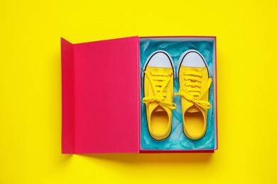 Photo of Comfortable sports shoes in cardboard box on yellow background, top view