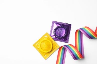 Photo of Colorful condoms and rainbow ribbon on white background, top view. LGBT concept