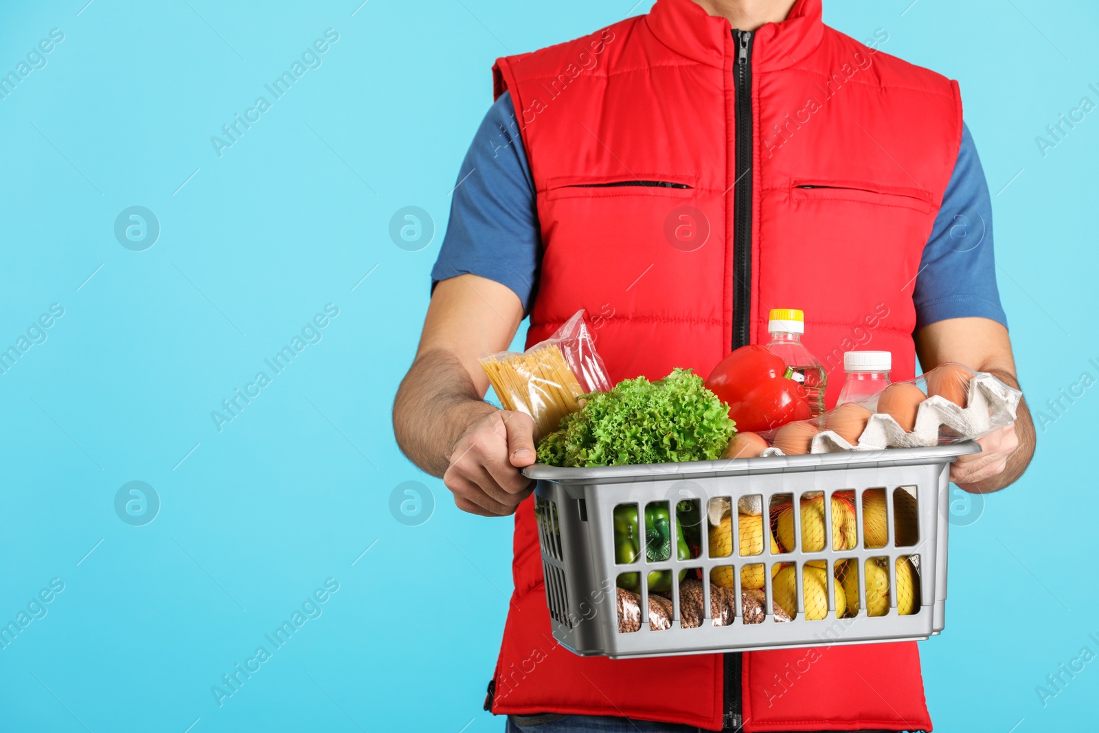 Photo of Man holding basket with fresh products on color background, closeup. Food delivery service