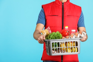 Photo of Man holding basket with fresh products on color background, closeup. Food delivery service