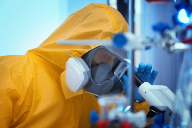 Photo of Scientist in chemical protective suit using microscope at laboratory. Virus research