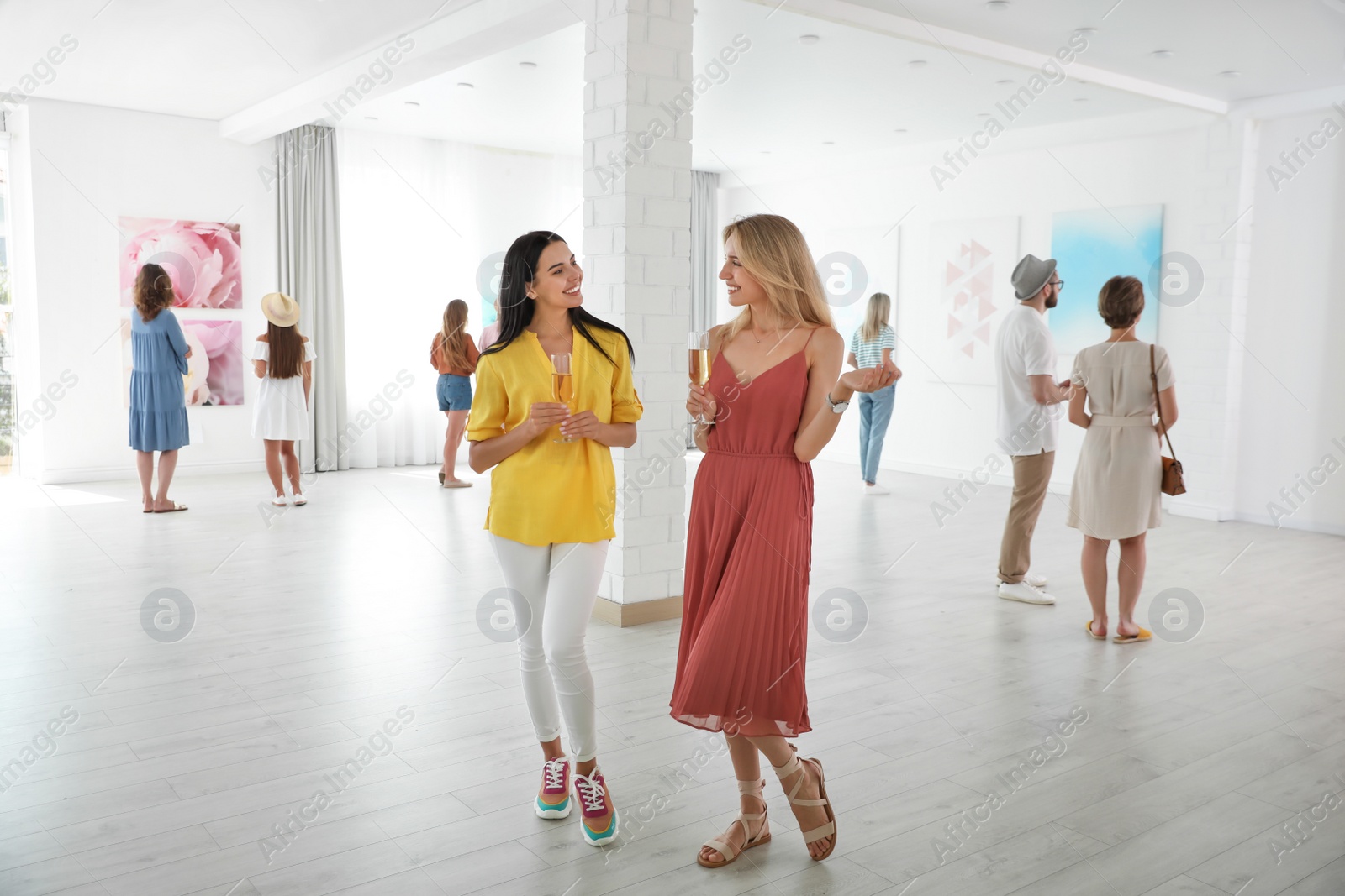 Photo of Young women with glasses of champagne at exhibition in art gallery