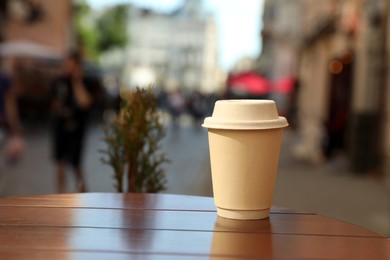 Photo of Cardboard takeaway coffee cup with lid on wooden table in city, space for text