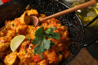 Photo of Delicious chicken curry in frying pan and spoon on table, closeup