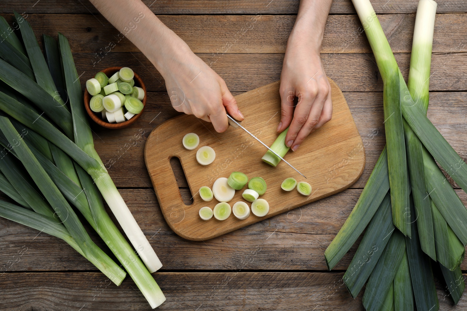 Photo of Woman cutting leek at wooden table, top view