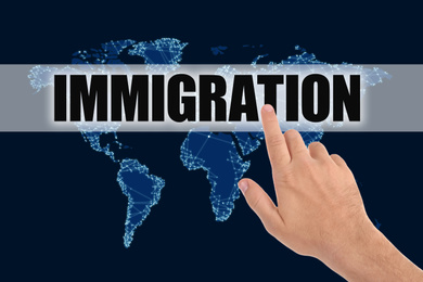 Image of Man pointing at word IMMIGRATION and world map on dark blue background, closeup