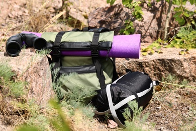 Backpack with sleeping bag, mat and binoculars outdoors on sunny day