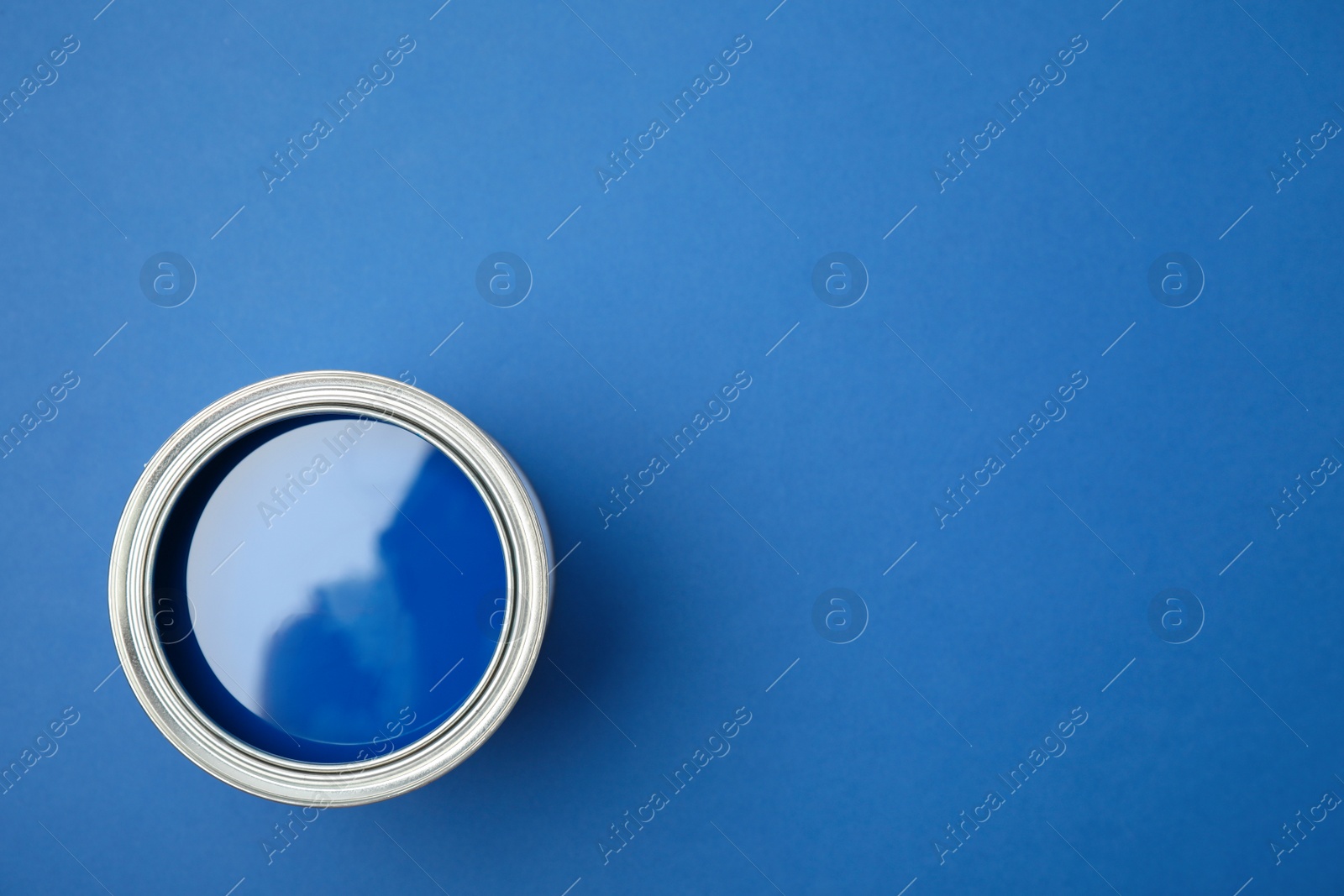 Photo of Open can of paint on blue background, top view. Space for text