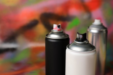 Cans of different graffiti spray paints on color background, closeup. Space for text