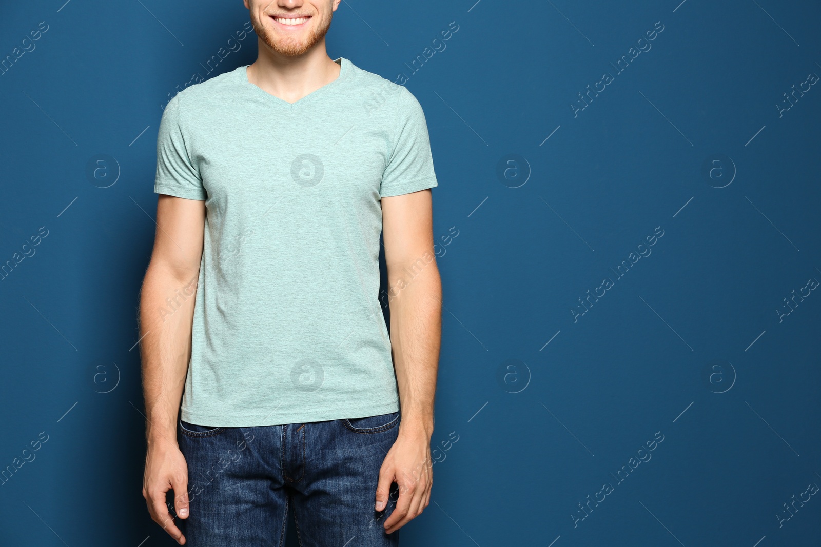 Photo of Young man wearing blank t-shirt on blue background, closeup. Mockup for design