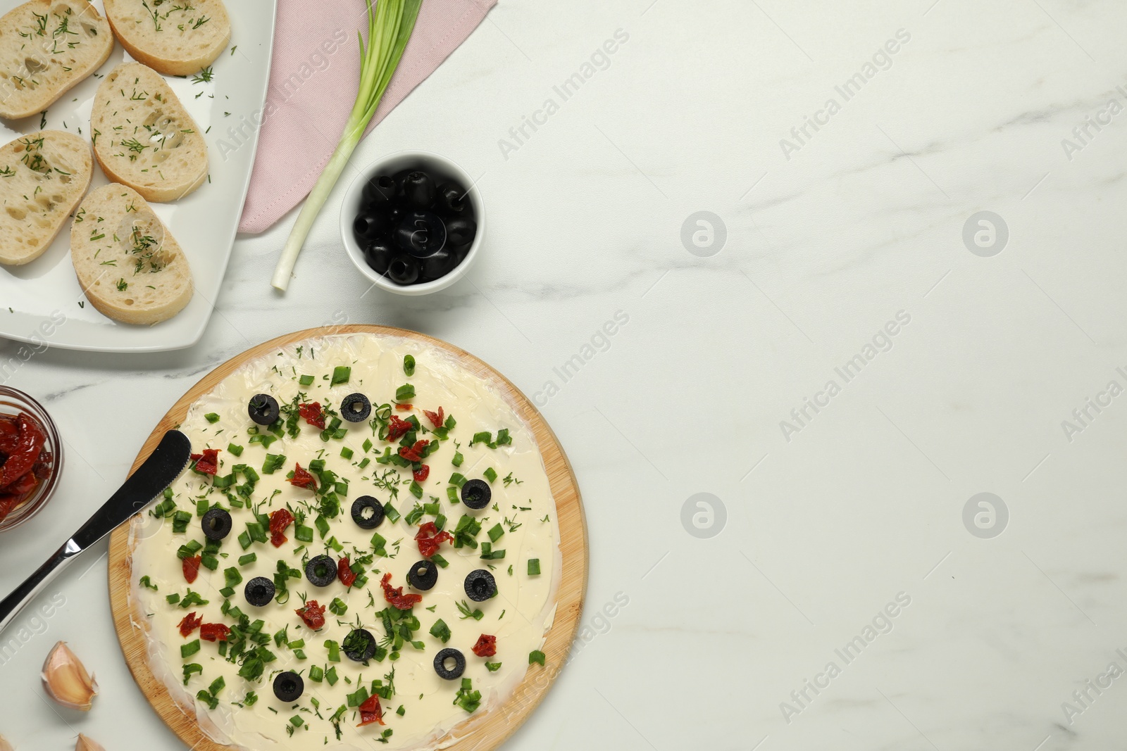 Photo of Fresh natural butter board with olives, bread and knife on white marble table, flat lay. Space for text