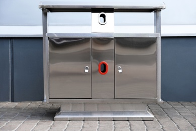 Photo of Modern metal recycling bin on street near building