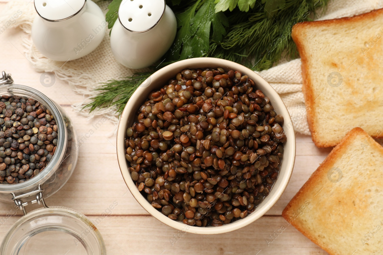 Photo of Delicious lentils in bowl served on wooden table, flat lay