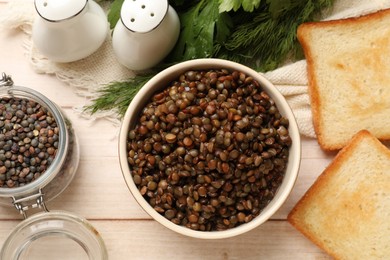 Photo of Delicious lentils in bowl served on wooden table, flat lay