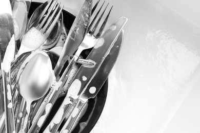 Photo of Washing silver spoons, forks and knives in foam, flat lay. Space for text