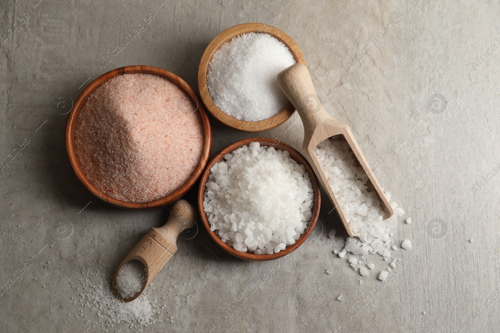 Photo of Different natural salt on grey textured table, flat lay