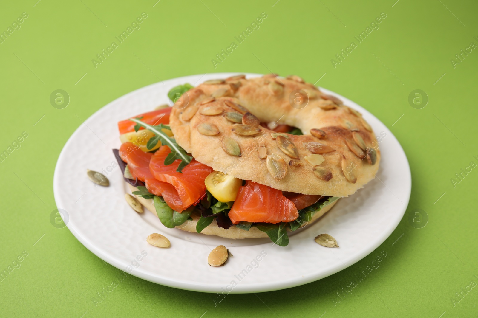 Photo of Tasty bagel with salmon and tomatoes on light green background