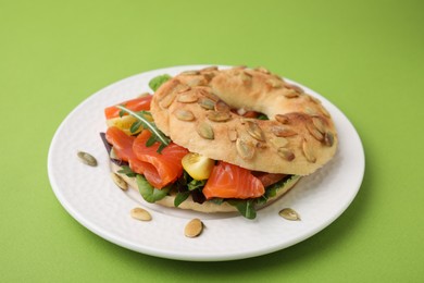 Tasty bagel with salmon and tomatoes on light green background