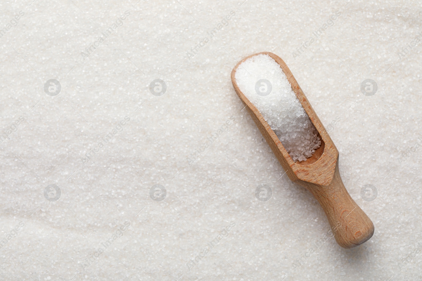 Photo of Wooden scoop on granulated sugar, top view. Space for text