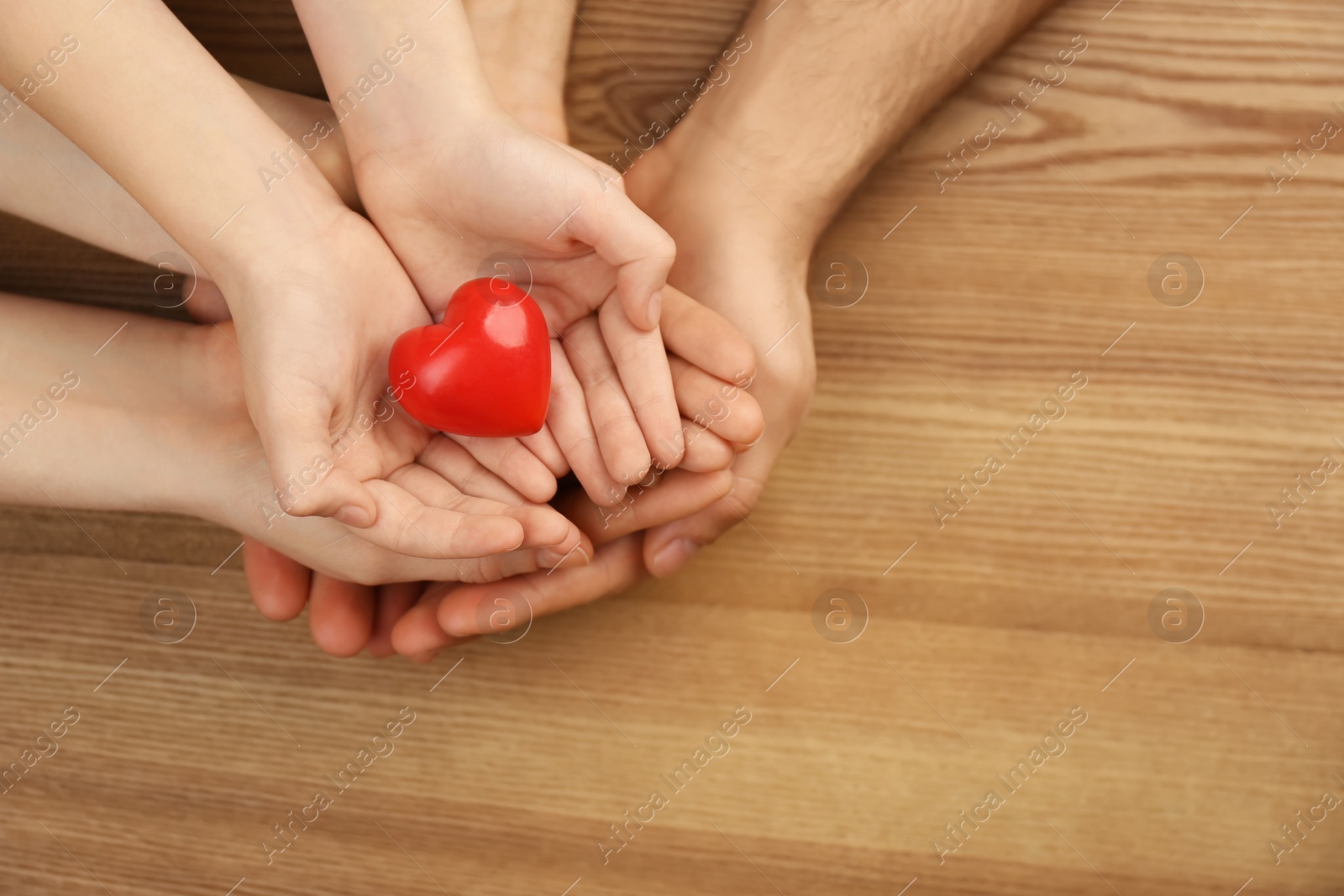 Photo of Top view of parents and kid holding red heart in hands at wooden table, space for text. Family day