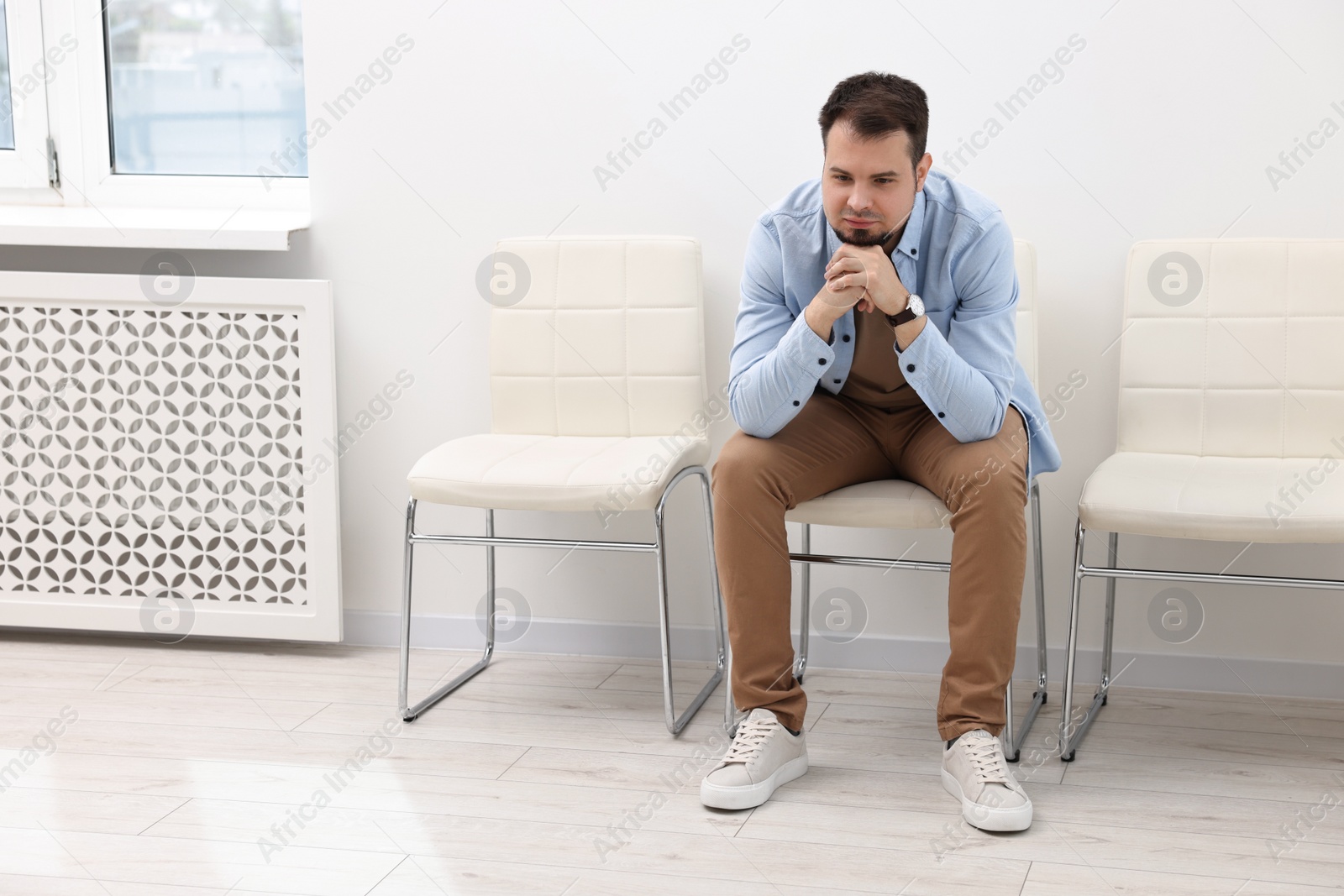 Photo of Man sitting on chair and waiting for appointment indoors