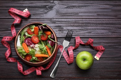 Bowl with fresh vegetable salad, fork, apple and measuring tape on wooden table, flat lay. Healthy diet concept