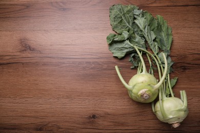 Whole ripe kohlrabies with leaves on wooden table, flat lay. Space for text
