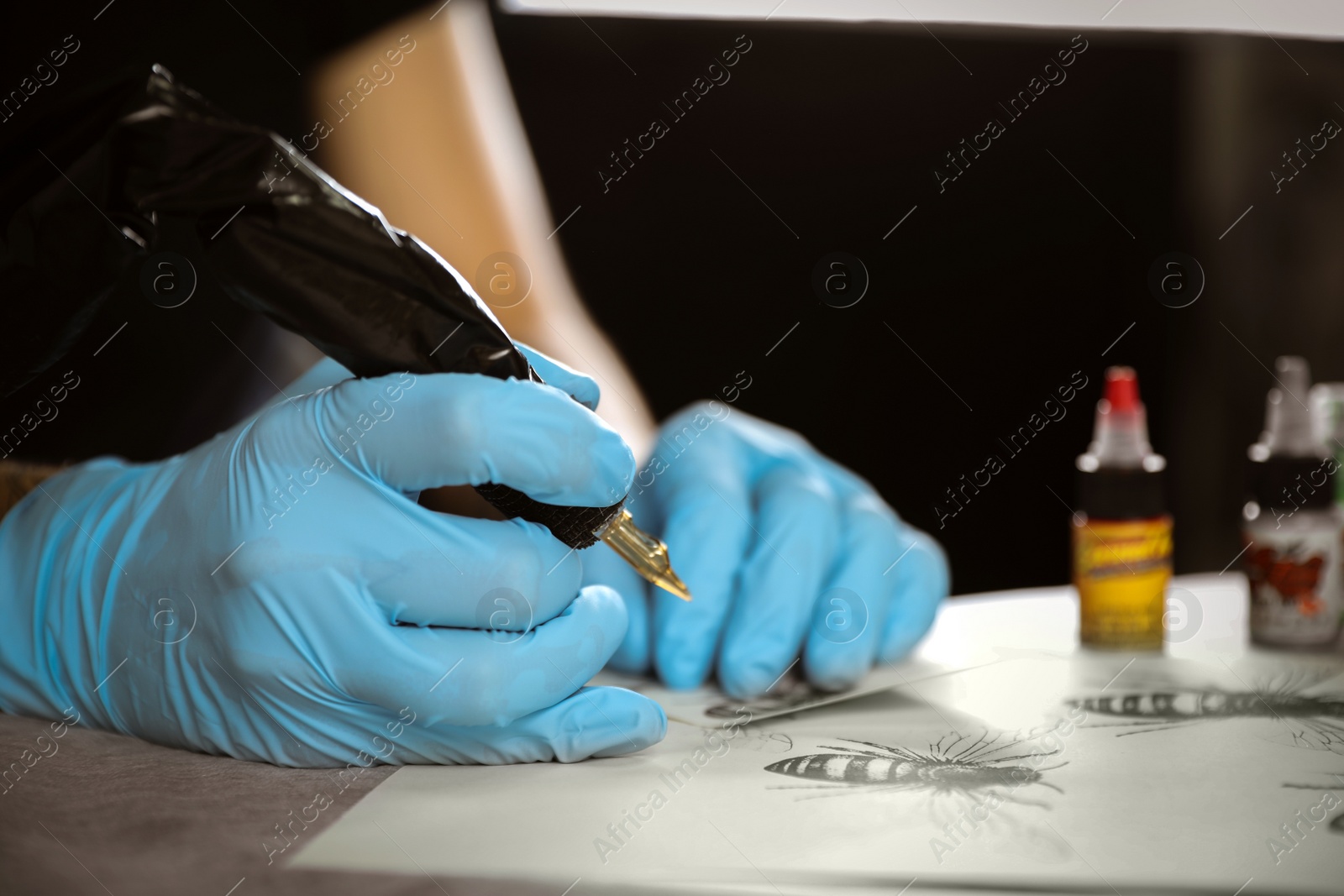 Photo of Master with tattoo machine, sketch and bottles of ink in salon, closeup