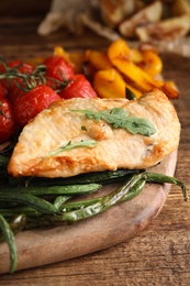 Photo of Delicious cooked chicken and vegetables on wooden table, closeup. Healthy meals from air fryer