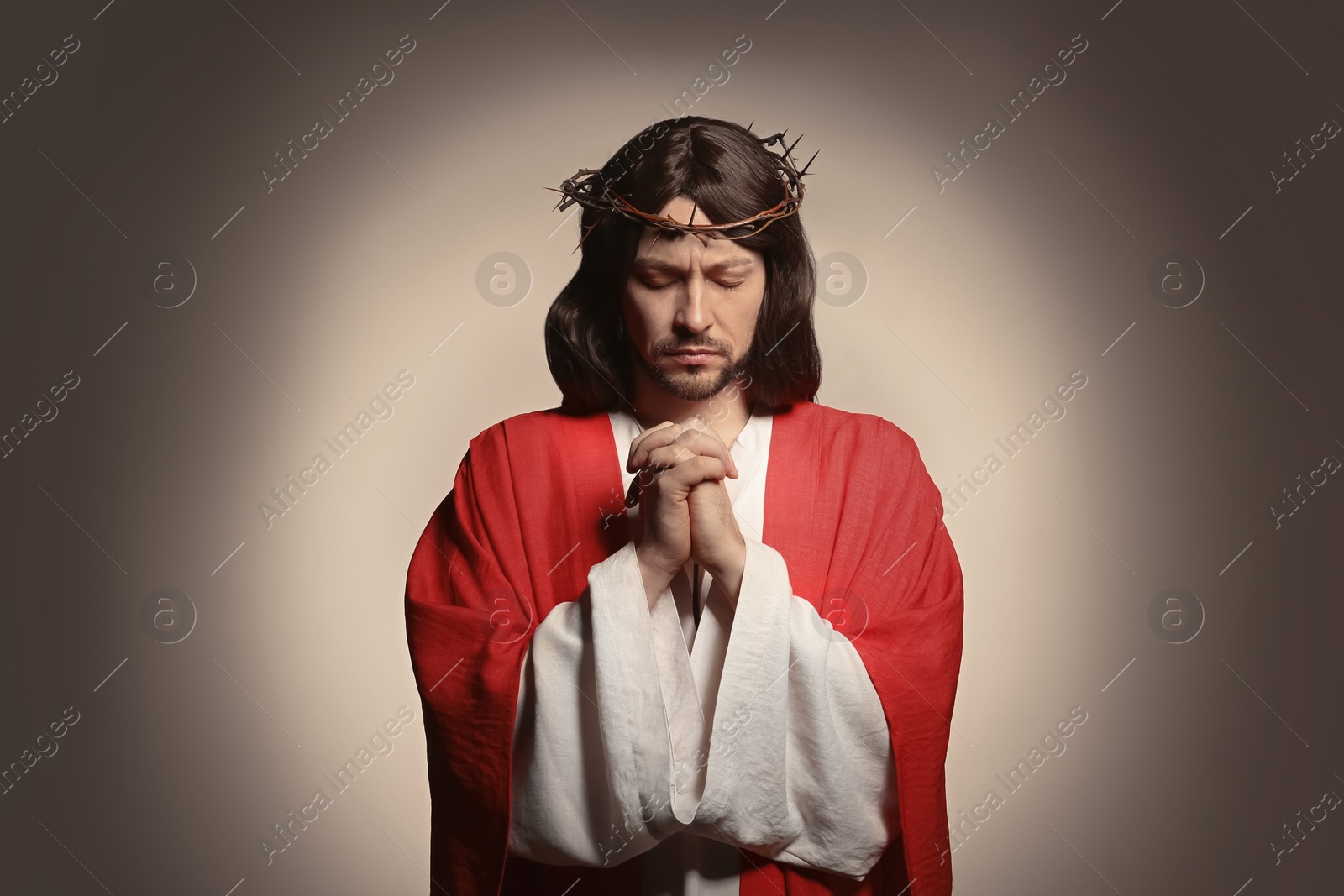 Photo of Jesus Christ with crown of thorns praying on beige background