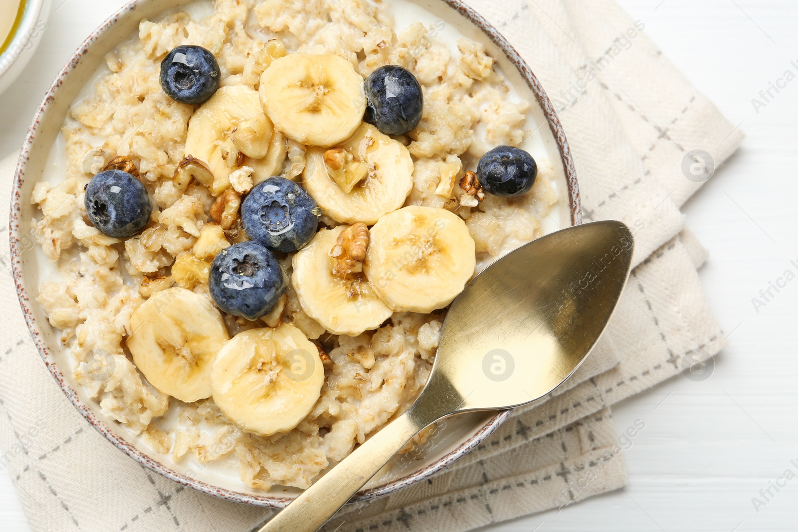 Photo of Tasty oatmeal with banana, blueberries, walnuts and honey served in bowl on white wooden table, top view