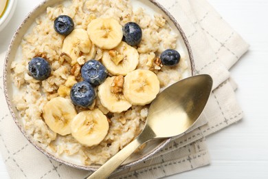 Tasty oatmeal with banana, blueberries, walnuts and honey served in bowl on white wooden table, top view