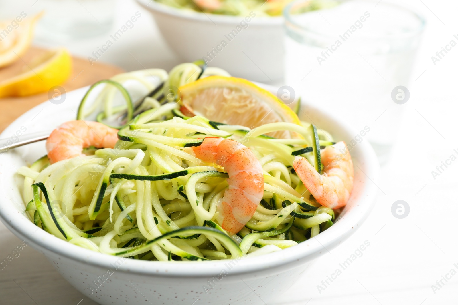 Photo of Delicious zucchini pasta with shrimps and lemon in bowl on white table, closeup