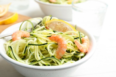 Photo of Delicious zucchini pasta with shrimps and lemon in bowl on white table, closeup