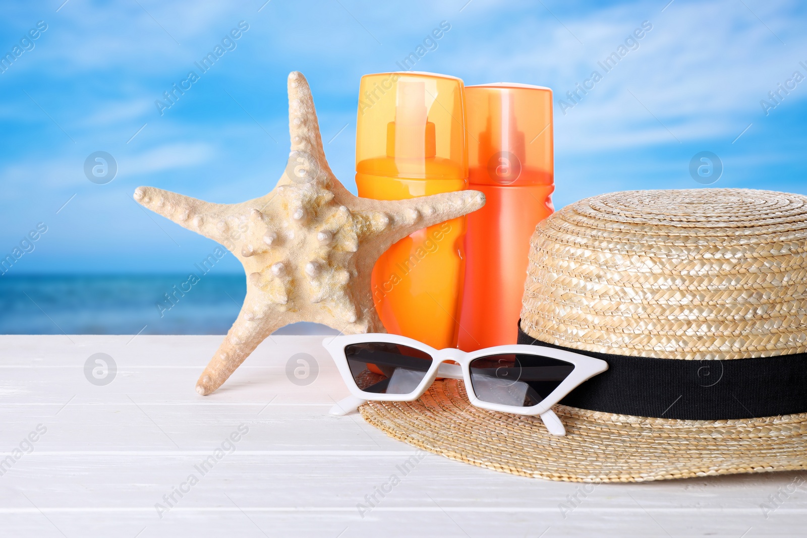 Image of Set of sun protection products and stylish accessories on white wooden table near sea