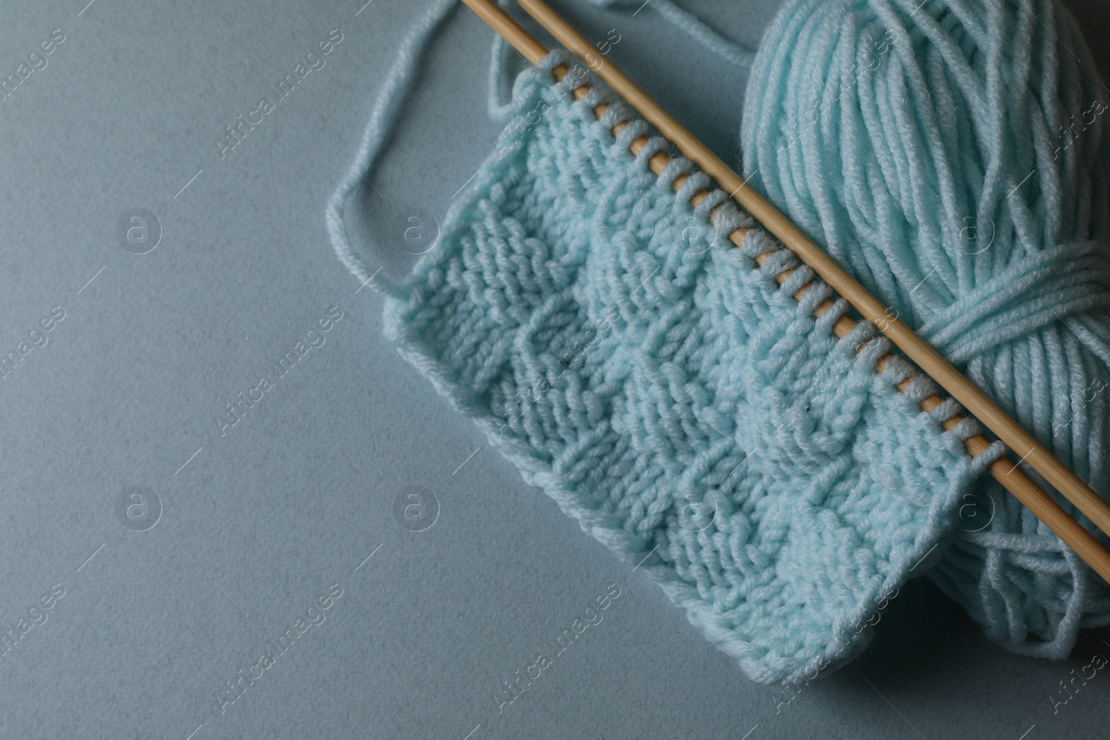 Photo of Soft turquoise knitting and needles on light blue background, top view. Space for text