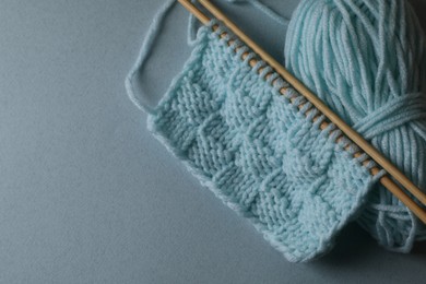 Soft turquoise knitting and needles on light blue background, top view. Space for text