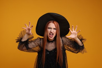 Photo of Young woman in scary witch costume on orange background. Halloween celebration