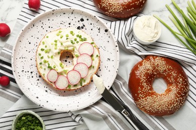 Photo of Delicious bagel with cream cheese, green onion and radish on table, flat lay