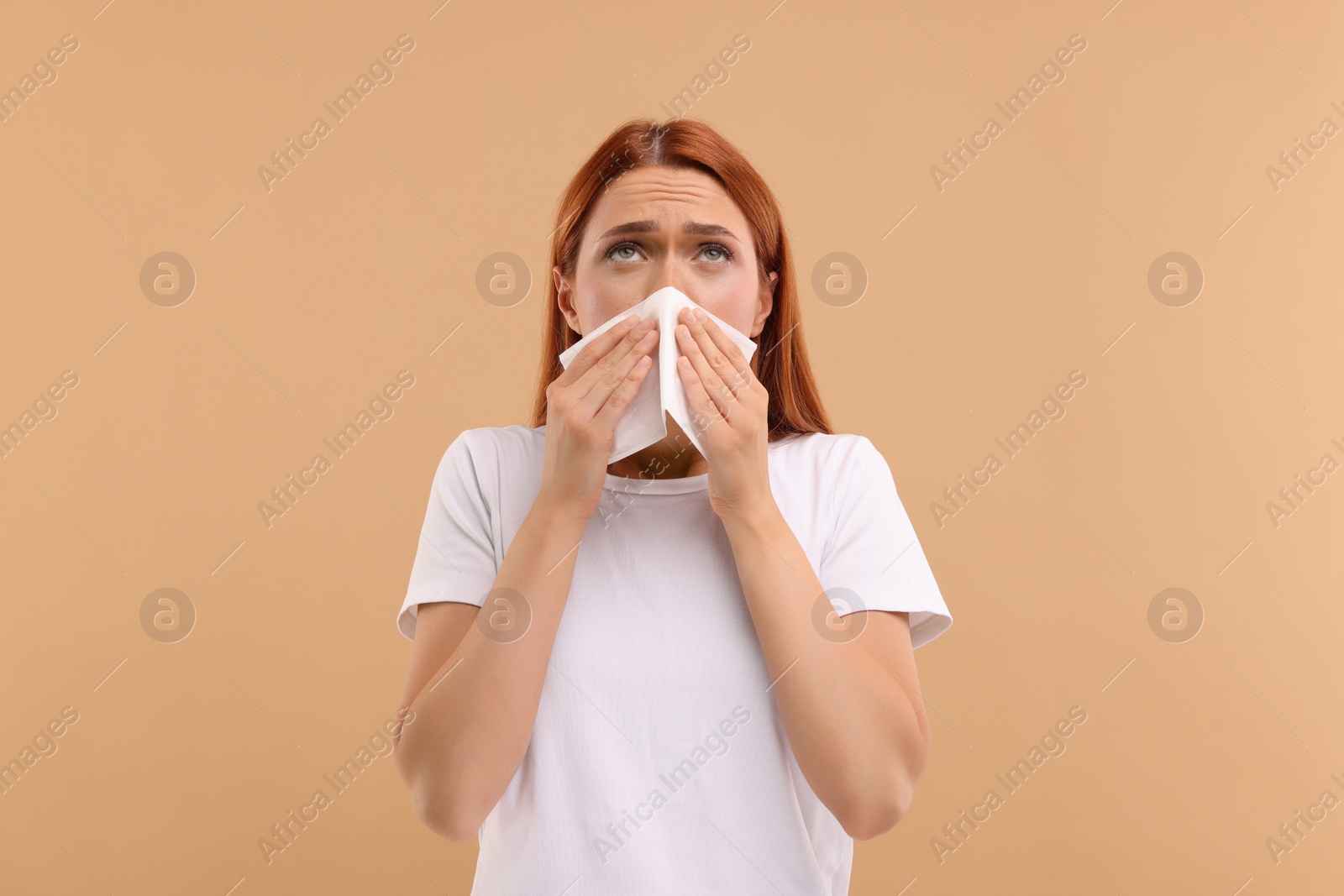 Photo of Suffering from allergy. Young woman with tissue sneezing on beige background