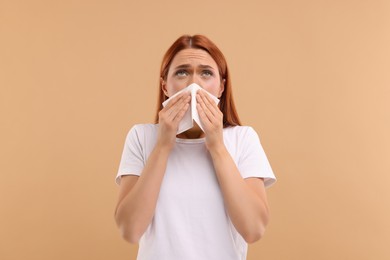 Photo of Suffering from allergy. Young woman with tissue sneezing on beige background