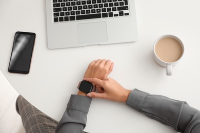 Image of Woman checking stylish smart watch at table, top view