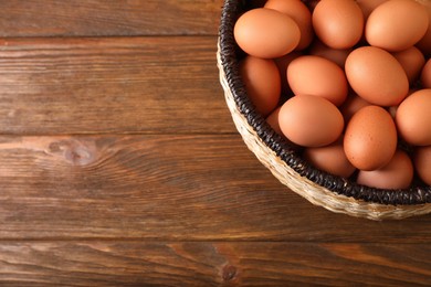 Raw chicken eggs in wicker basket on wooden table, top view. Space for text