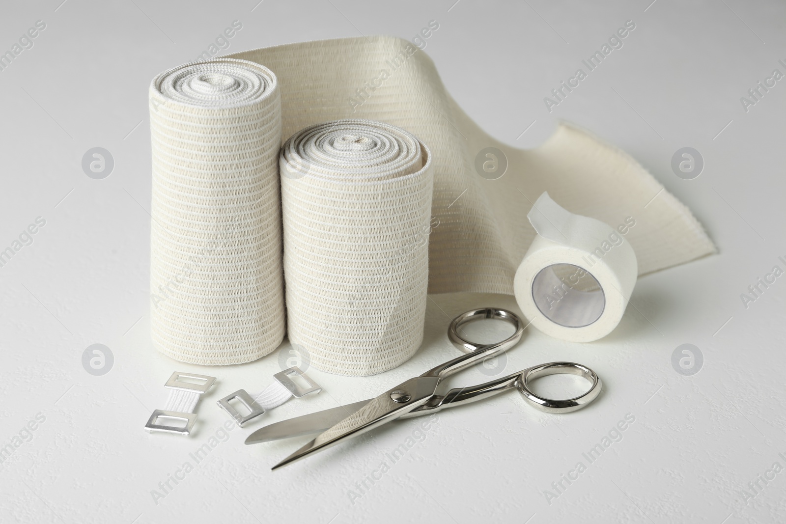 Photo of Medical bandage rolls, sticking plaster and scissors on white table