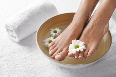 Photo of Closeup view of woman soaking her feet in dish with water and flowers on white towel, space for text. Spa treatment