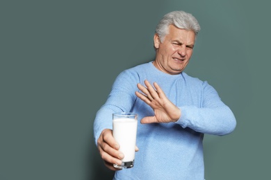 Mature man with dairy allergy holding glass of milk on color background