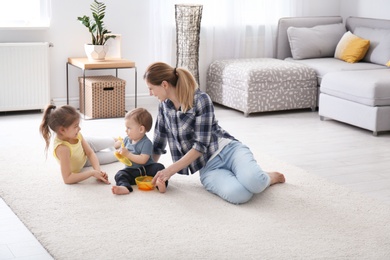 Mother with cute little children sitting on cozy carpet at home