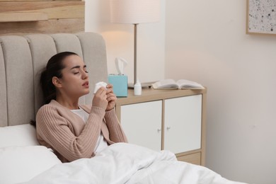 Photo of Sick young woman with napkins and nasal spray in bed at home