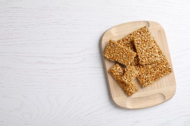 Photo of Wooden board with delicious kozinaki pieces on white table, top view. Space for text