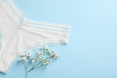 Photo of White women's underwear and flowers on light blue background, flat lay. Space for text